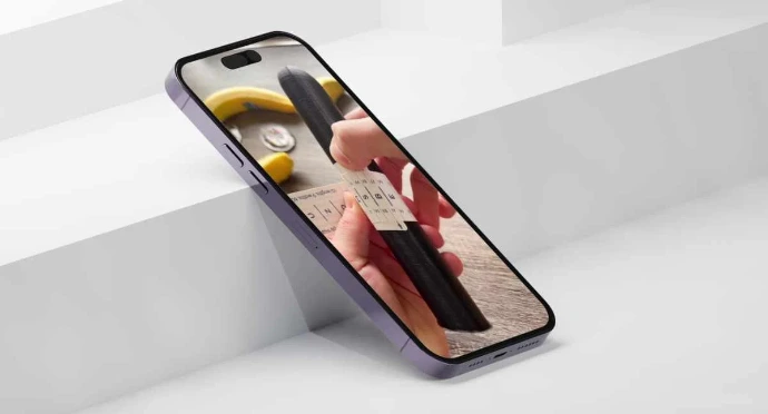 Mobile Sizing Tool A close-up of a smartphone leaning against a white geometric surface. The screen displays a person using a paper measuring tool—marked with letters and numbers—around a dark, cylindrical object to determine the correct custom condom size.